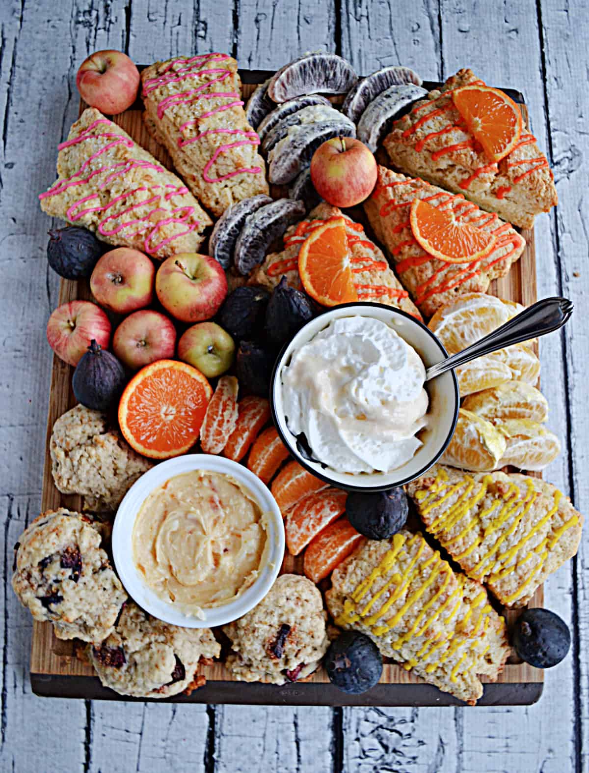 A board covered with fruit, scones, and spreads. 