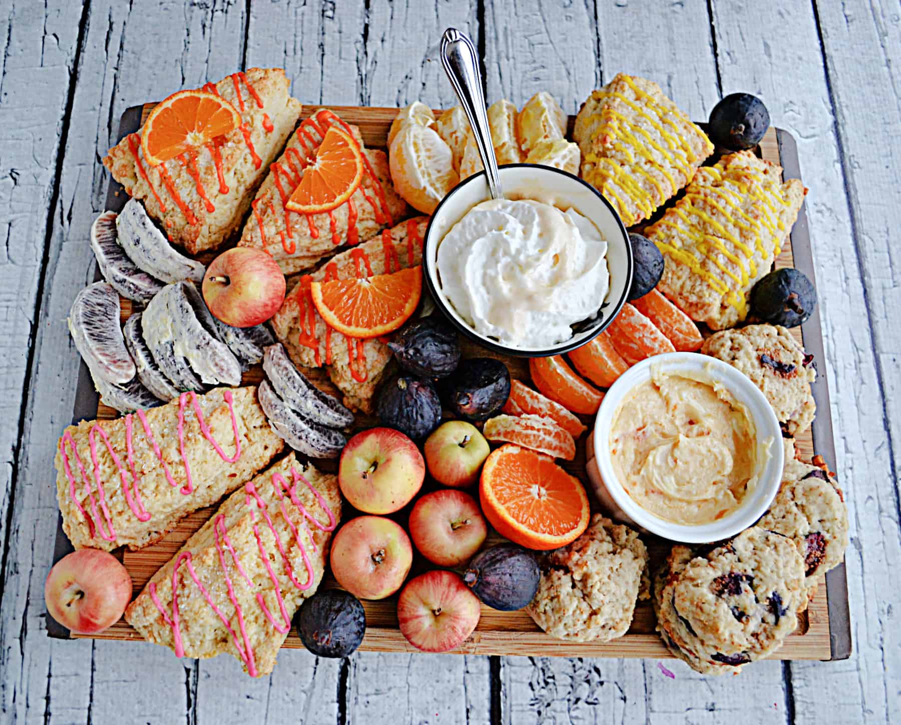 A breakfast board with scones, fresh fruits, and spreads.