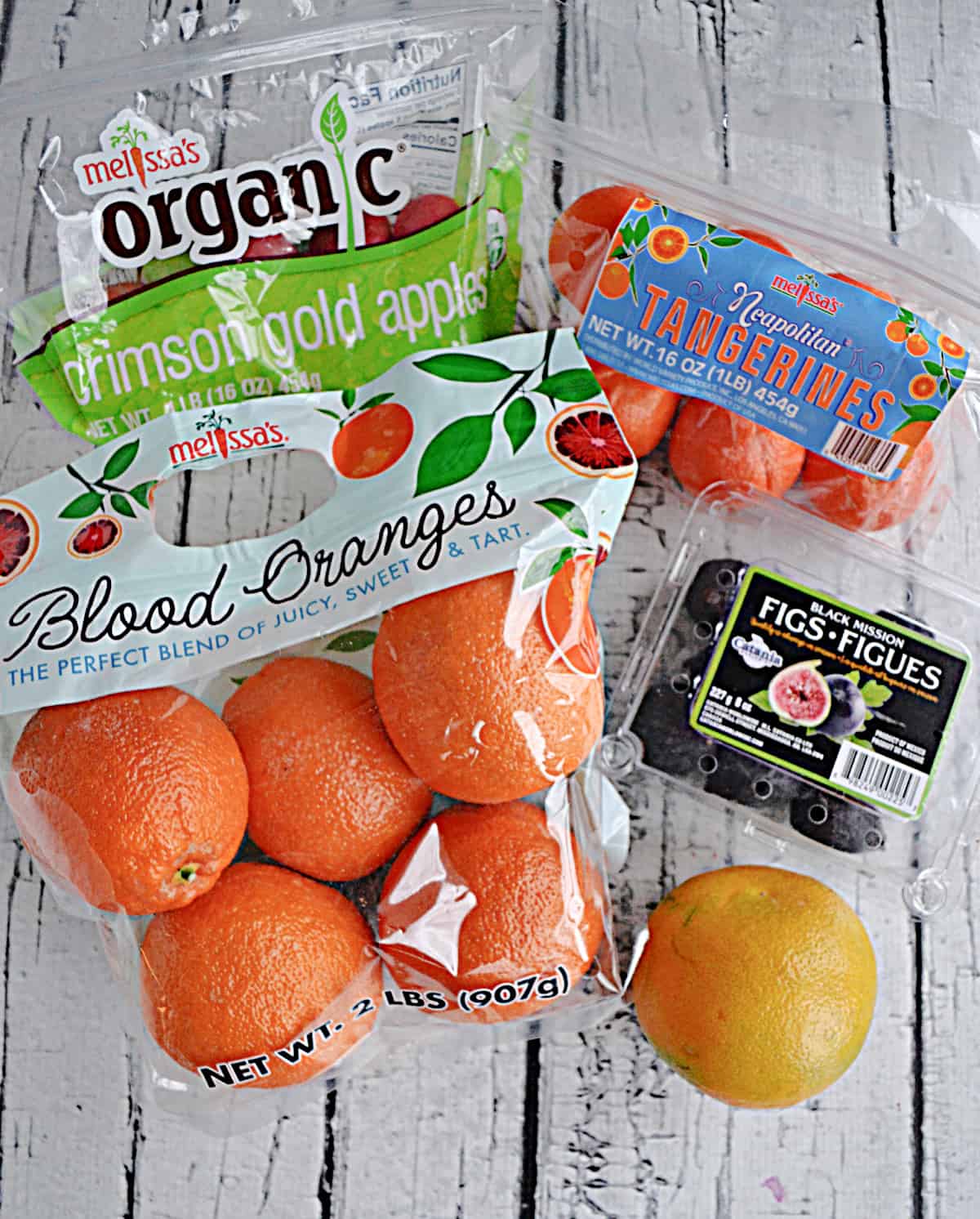 A bag of tangerines, oranges, apples, a package of figs, and a grapefruit.
