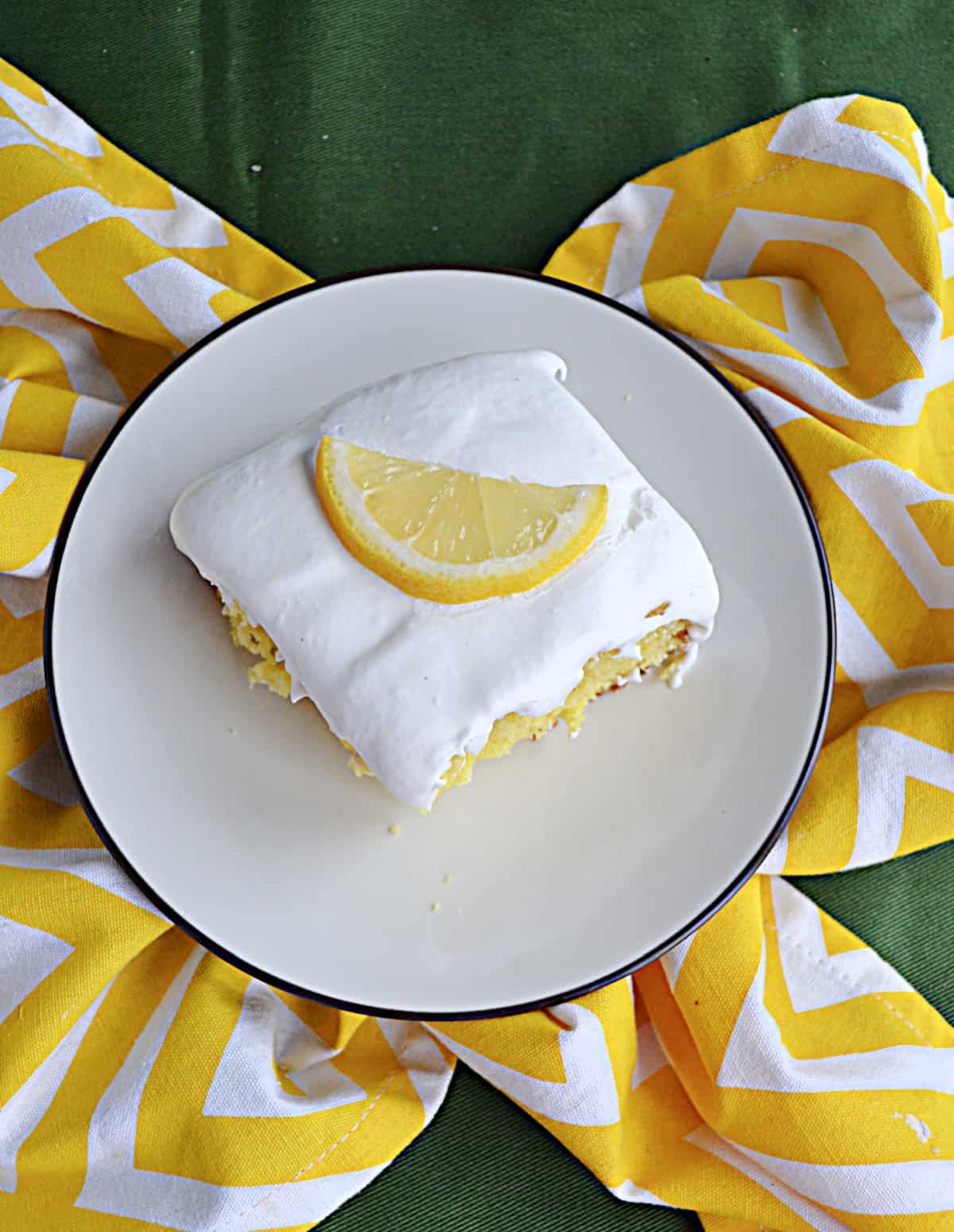 A slice of lemon cake on a plate with a lemon wedge on top.