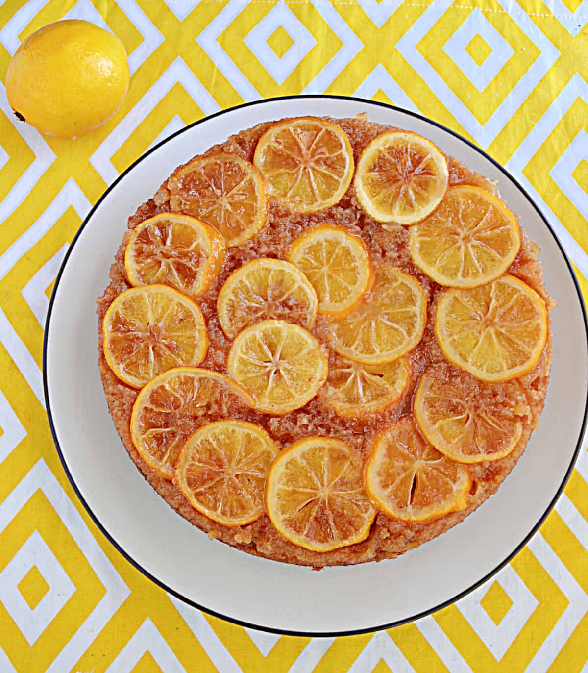 A lemon upside down cake with lemon slices on top and a lemon beside it.