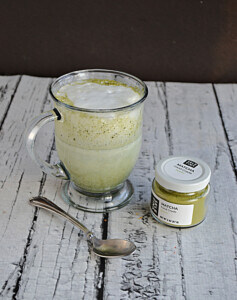 A mug of matcha with milk on top and a jar of matcha sitting next to it.