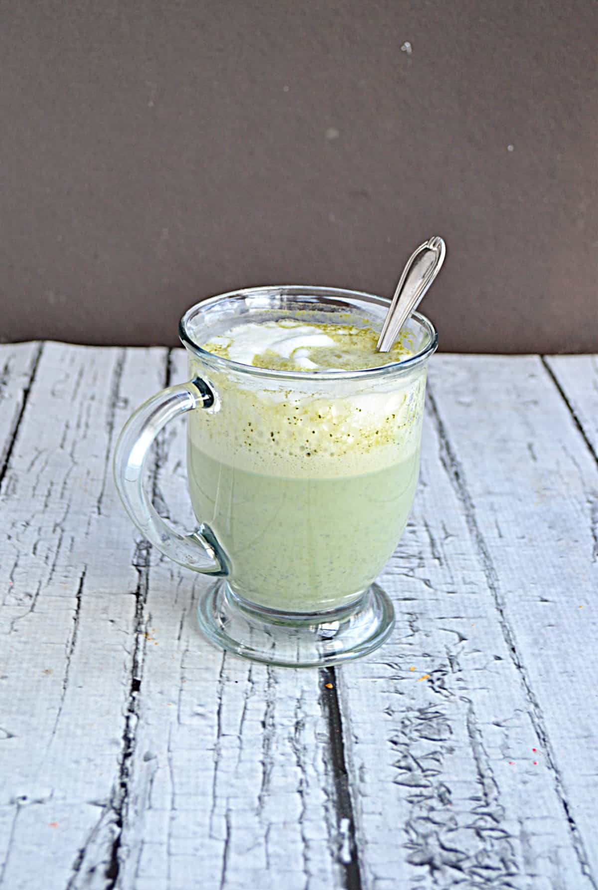 A mug of green tea matcha latte with a spoon in it.
