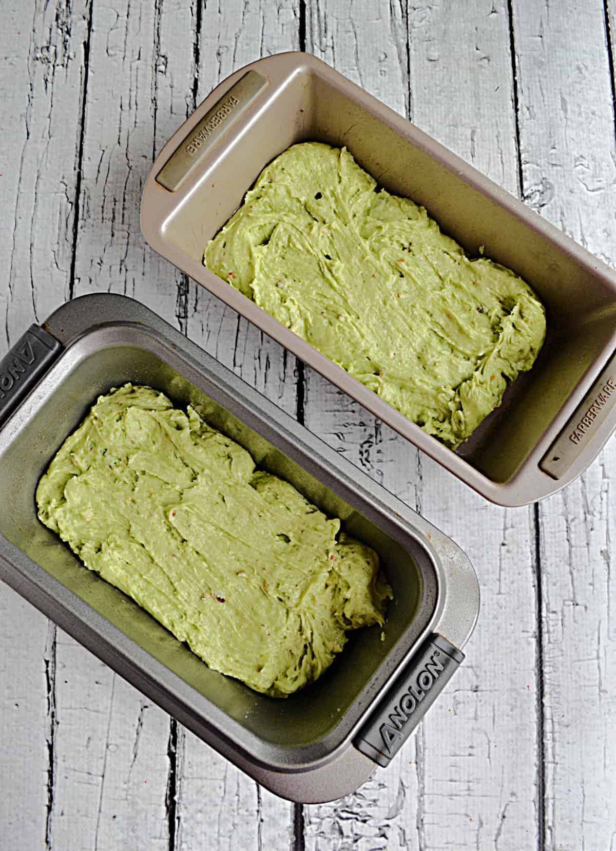 Two loaf pans filled with pistachio cake batter.