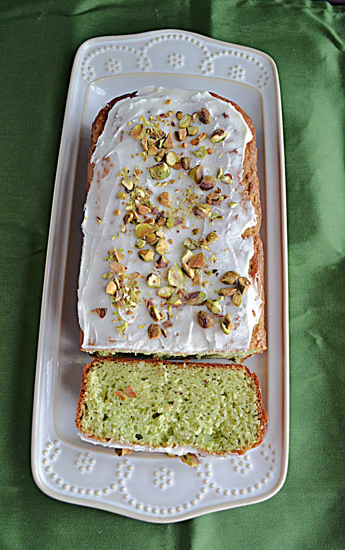 Pistachio Loaf Cake on a platter with a slice cut off of it. 