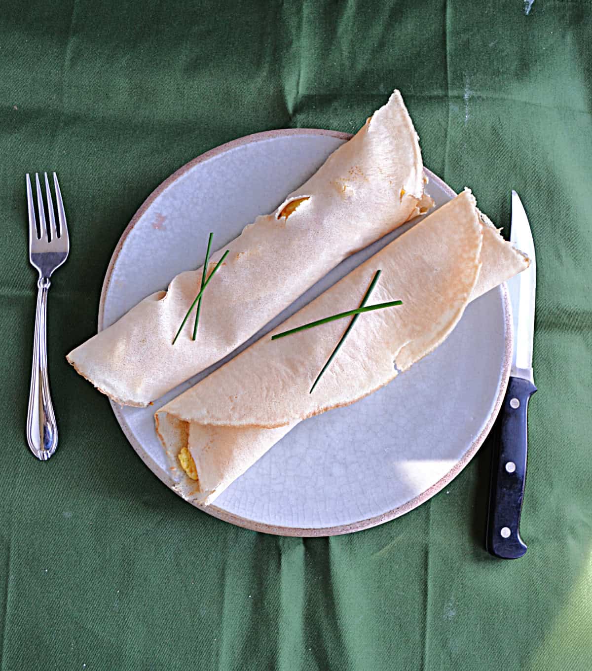 A plate with two crepes, a fork, and a knife.