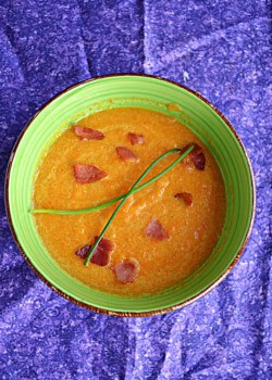 A bowl of creamy carrot soup with bacon and chives on top.