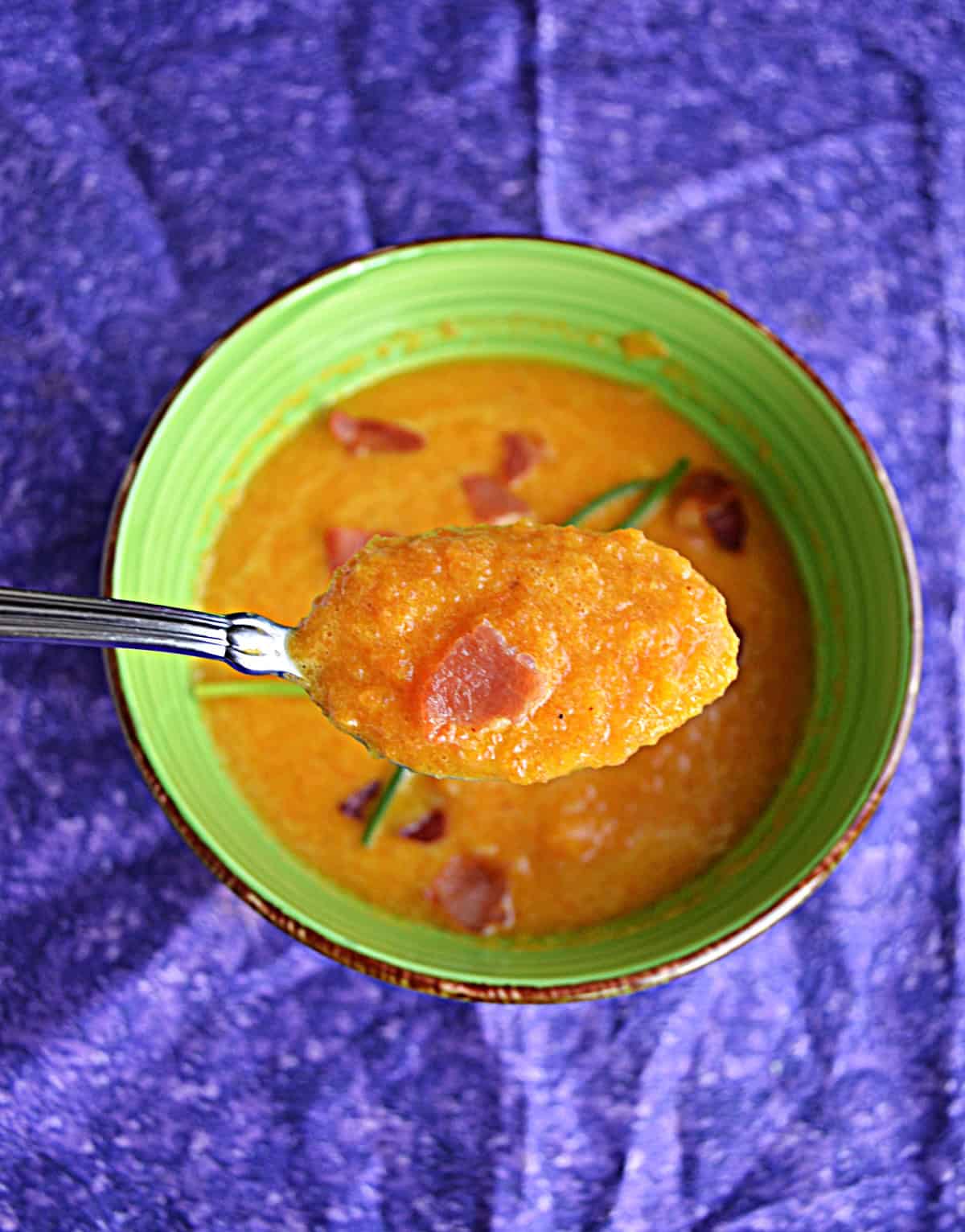 A bowl of carrot soup with a spoonful of the soup on a spoon.