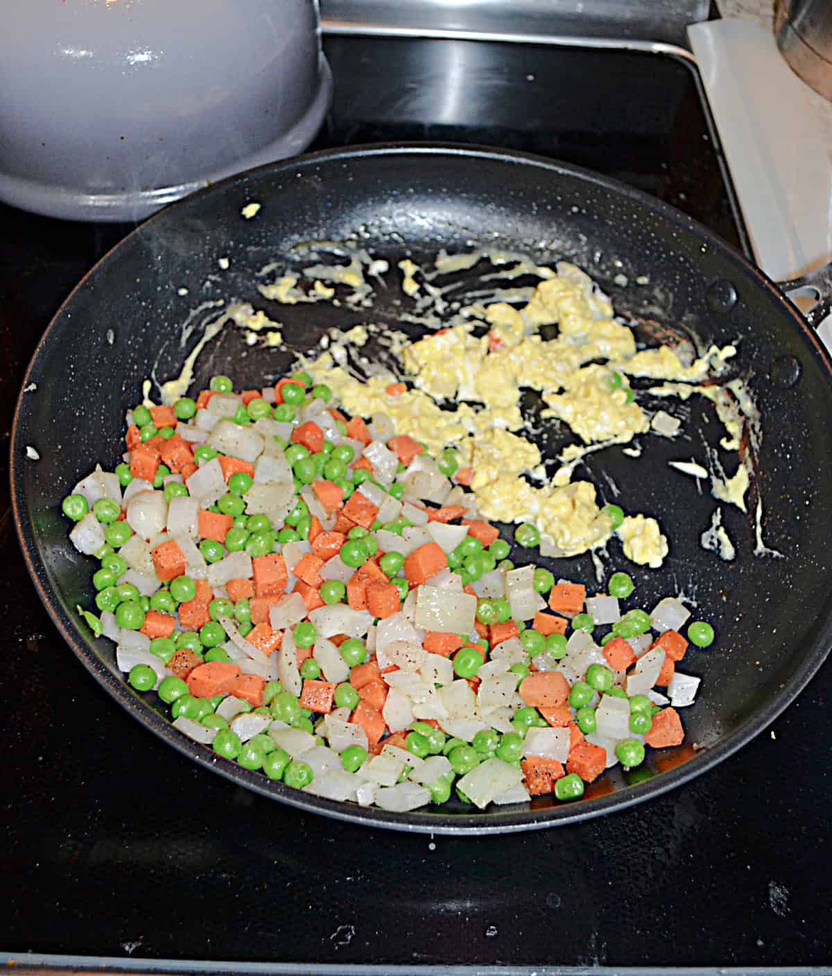 A skillet with egg in half of it and vegetables in the other half.