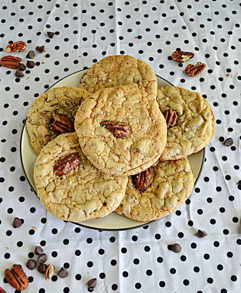 A plate of Bourbon Pecan Chocolate Chip Cookies with pecans and chocolate chips sprinkled around the plate.