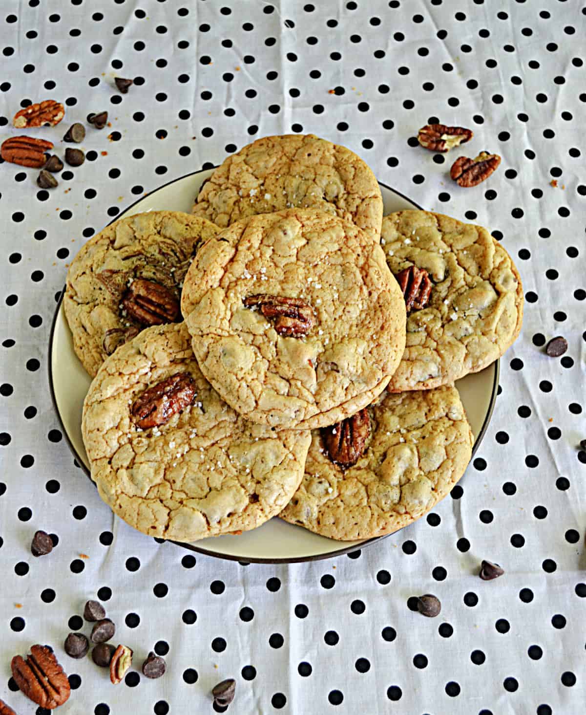 A plate of Bourbon Pecan Chocolate Chip Cookies with pecans and chocolate chips sprinkled around the plate.