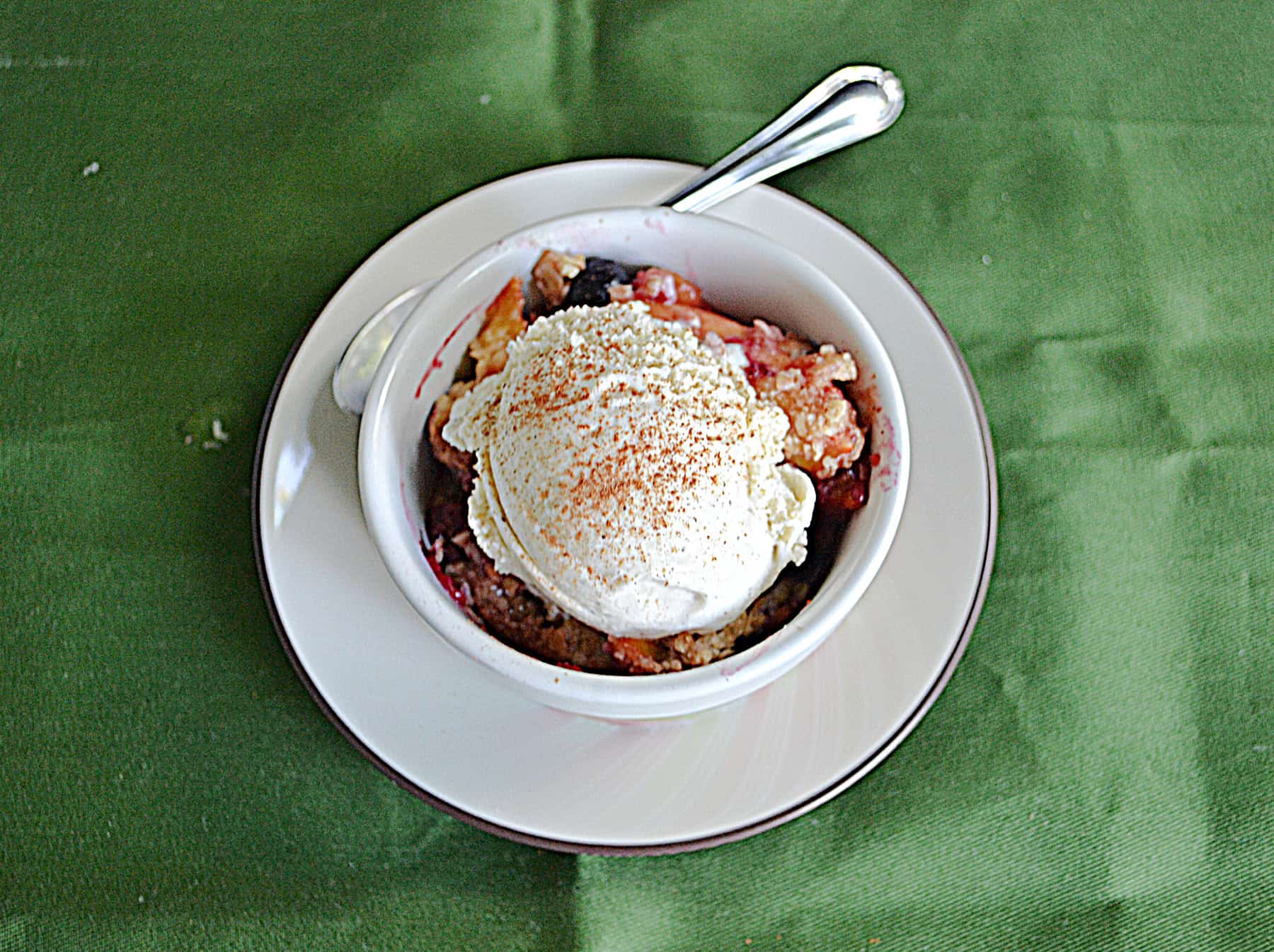 A bowl of peach crisp with ice cream on top.