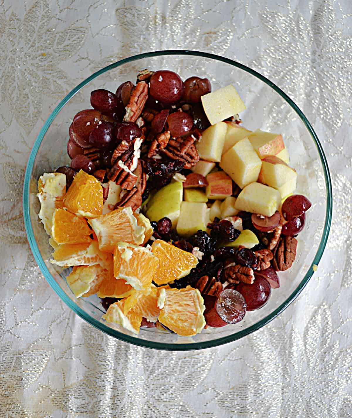 A bowl with oranges, apples, grapes, cranberries, and pecans.