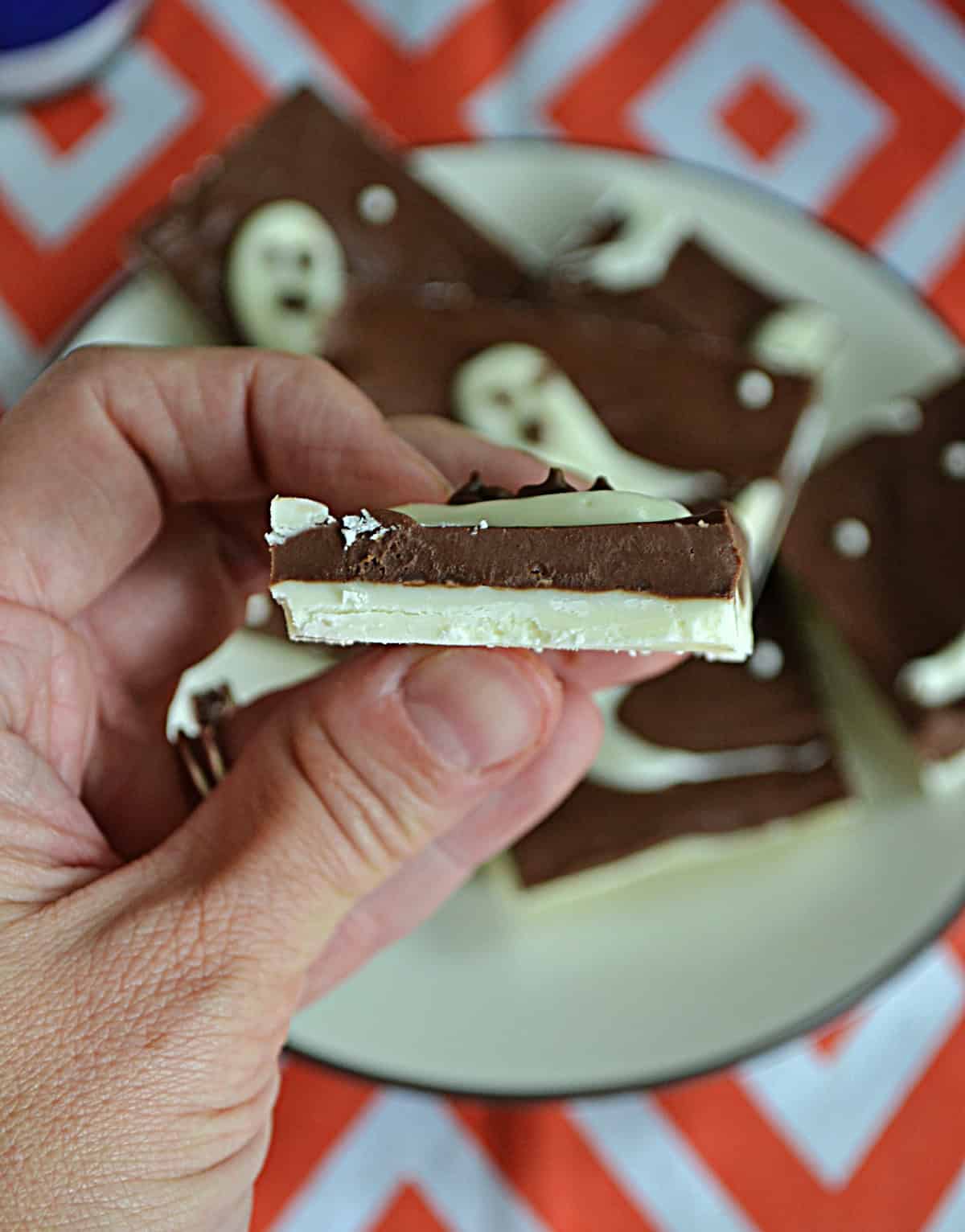 A hand holding a piece of bark that shows a layer of milk chocolate and a layer of white chocolate.