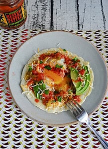 A crepe topped with a runny egg, avocado, salsa, and cheese with a fork cutting into the egg.