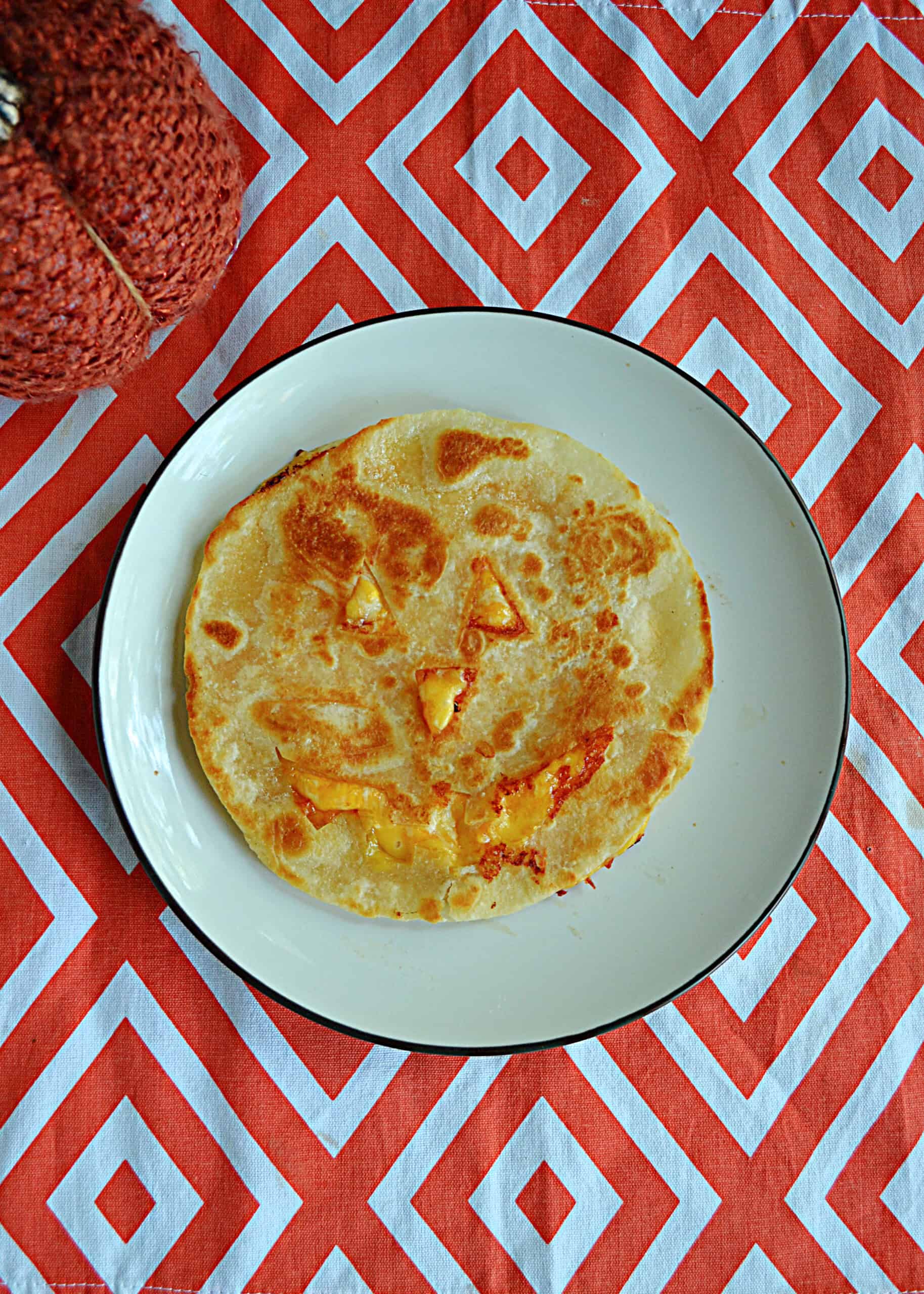 A quesadilla on a plate with a Jack-o-lantern face cut out of it.