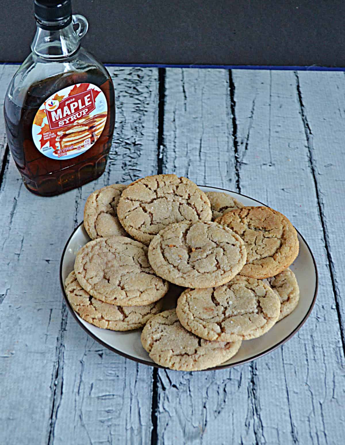 A plate of maple snickerdoodle cookies with a bottle of maple syrup.
