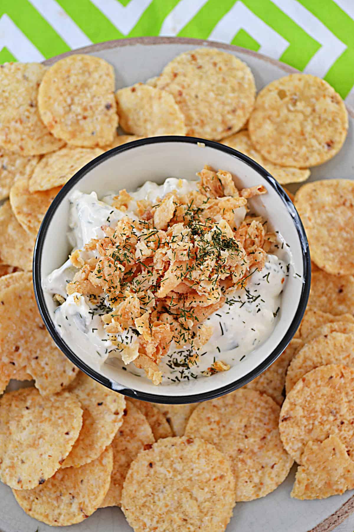 A close up of a bowl of pickle dip in the middle of a bunch of tortilla chips.