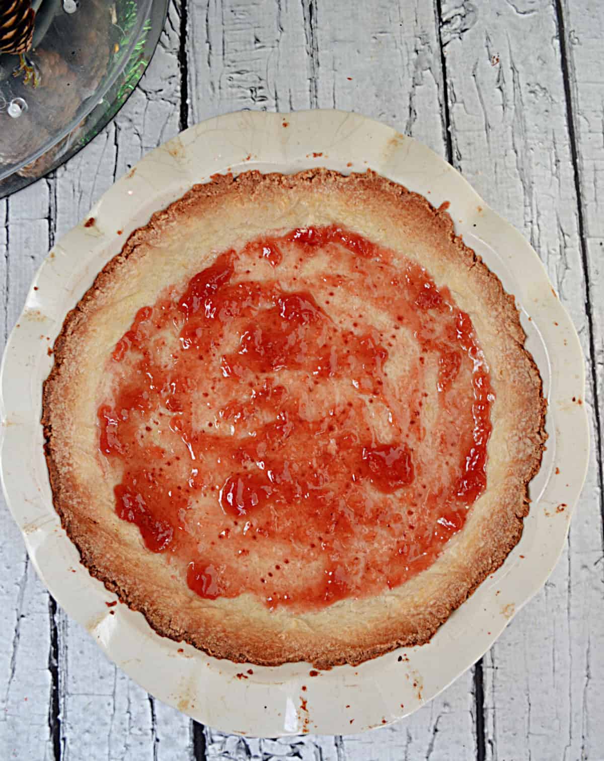 A baked pie crust with jam in the bottom of the pan.
