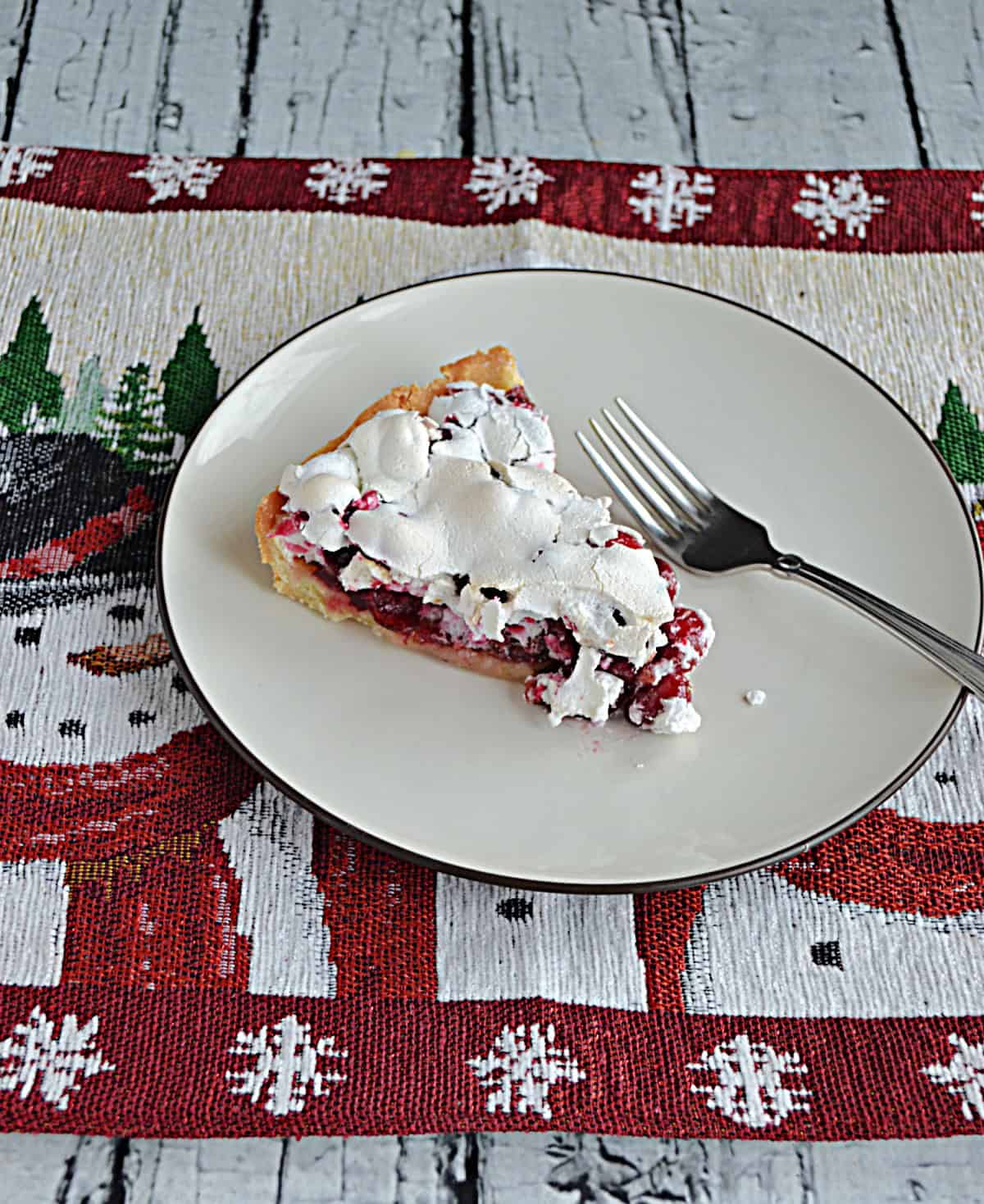 A plate with a slice of cranberry and meringue tart with a fork on the plate.