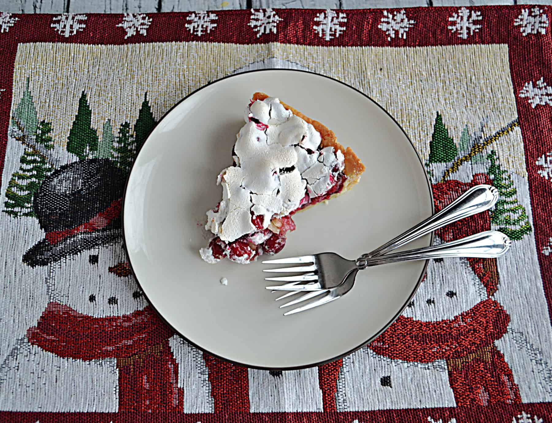 A plate with a slice of cranberry meringue pie with 2 forks on the plate.