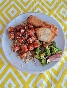 A plate of sesame tofu, broccoli, and an egg roll.