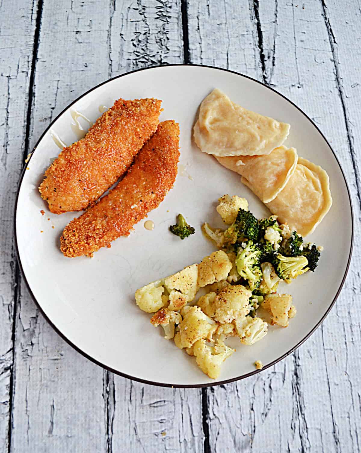 A dinner plate with chicken strips, cauliflower, and pierogi on it.