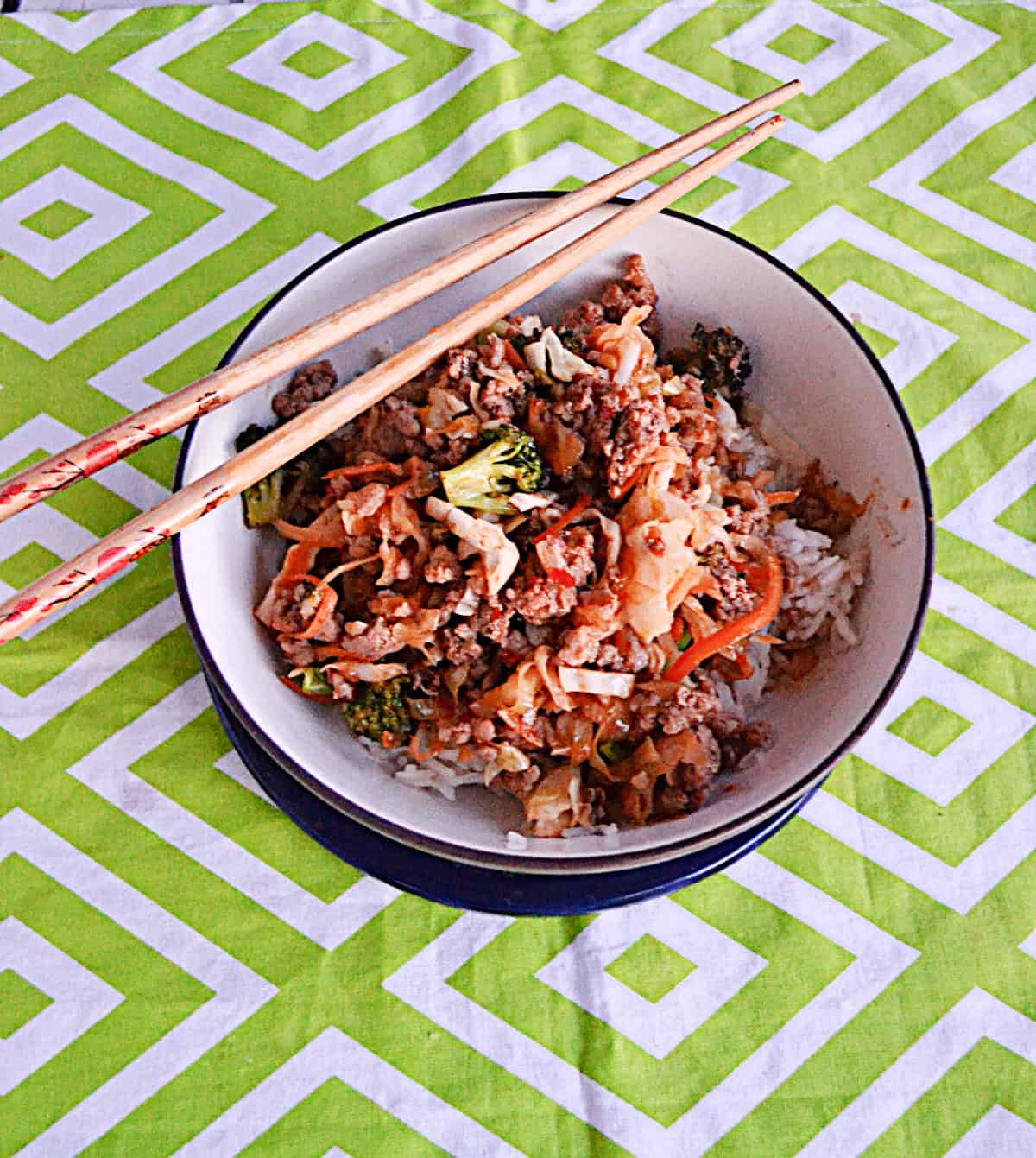 A bowl of ground pork, cabbage, and broccoli with chop sticks on the edge.
