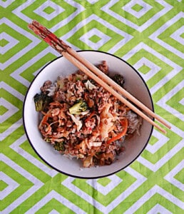 A bowl of pork and vegetables with chopsticks on the rim.