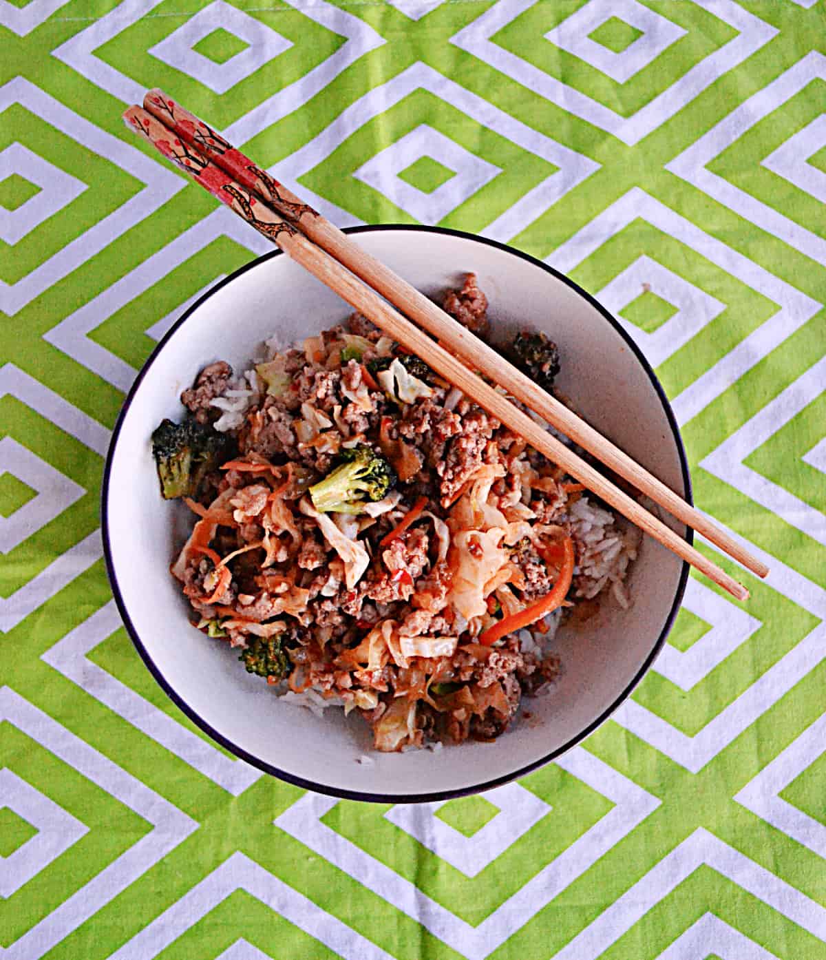 A bowl of pork and vegetables with chopsticks on the rim.