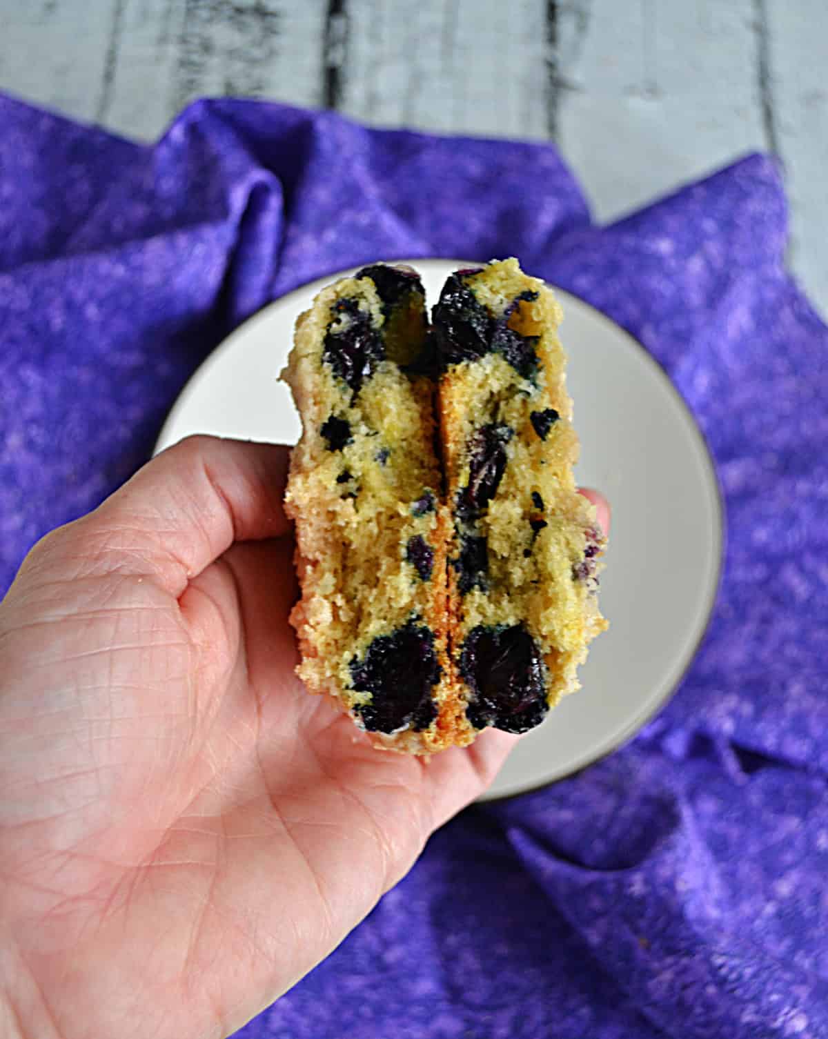 A hand holding a blueberry muffin cookie broken in half.