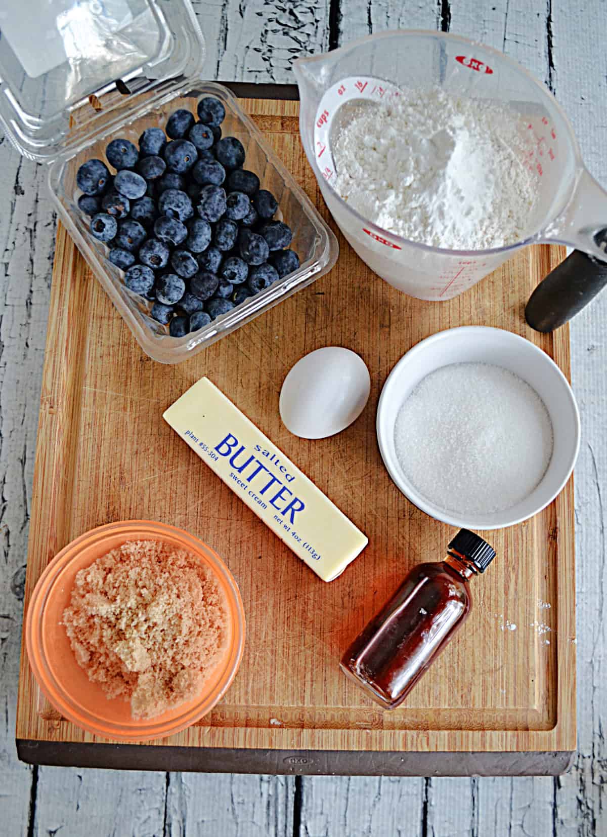 A wooden cutting board with blueberries, butter, sugar, and flour