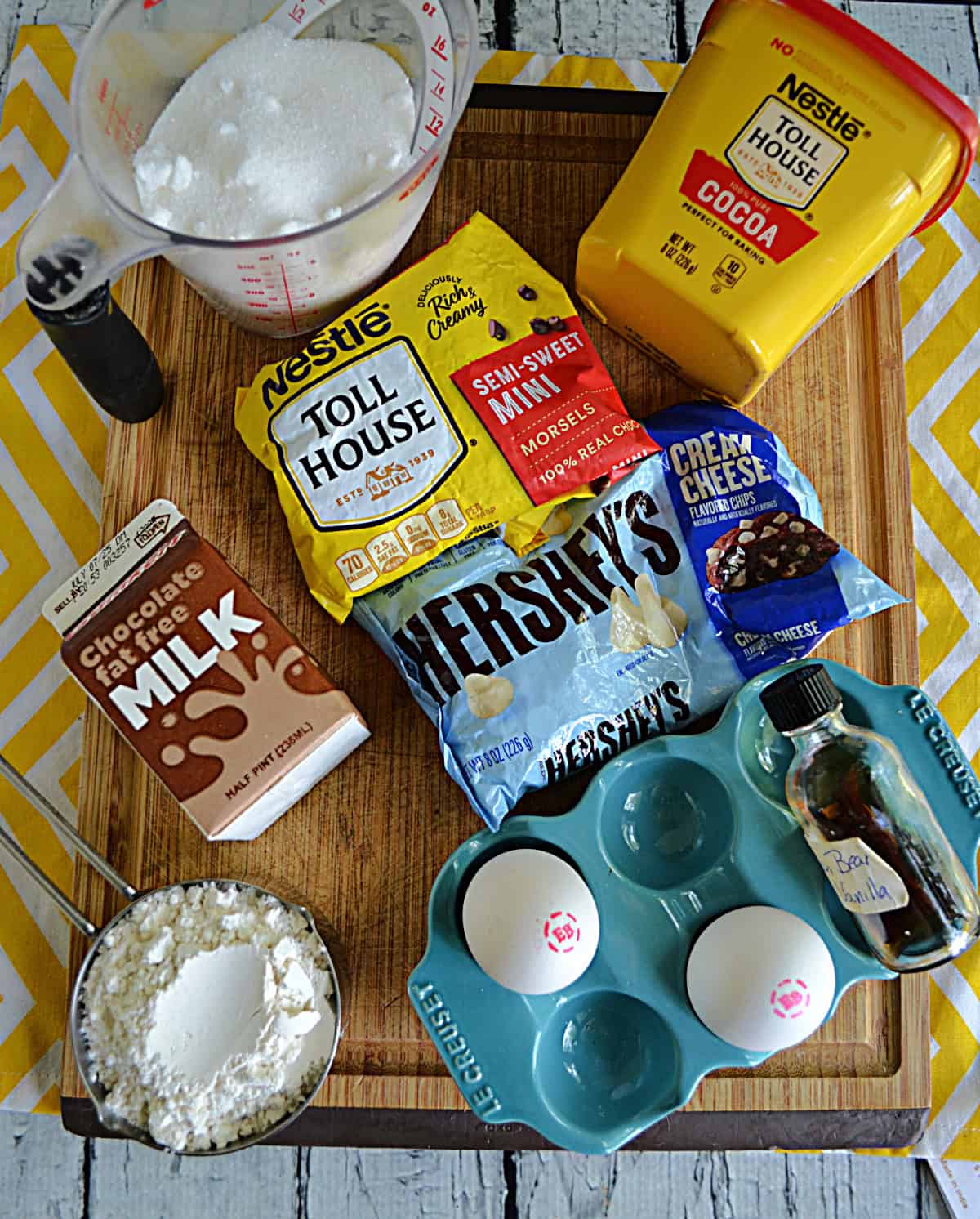Cutting board with chocolate hips, chocolate milk, cocoa powder, eggs, flour, sugar,and butter.