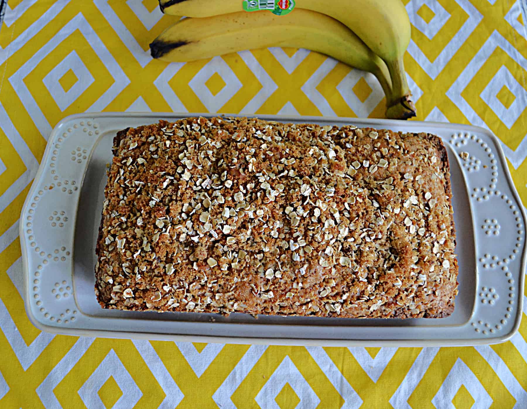 Banana Bread on a platter with bananas in the background.