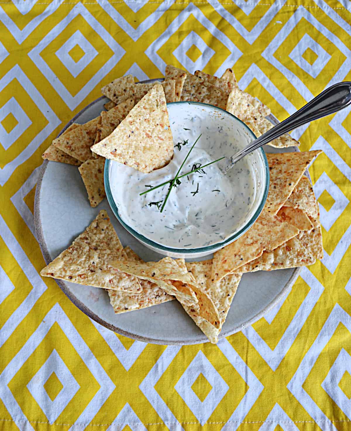 A plate of tortilla chips with a bowl of dip in the middle. The bowl of dip has a chip and a spoon in it.