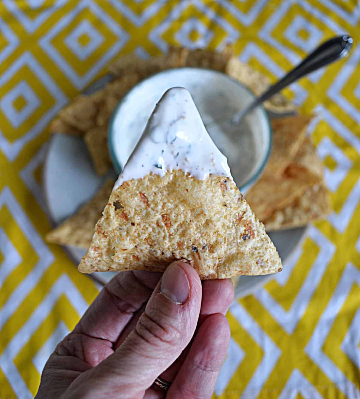 A close up of a hand holding a chip with dip on it.