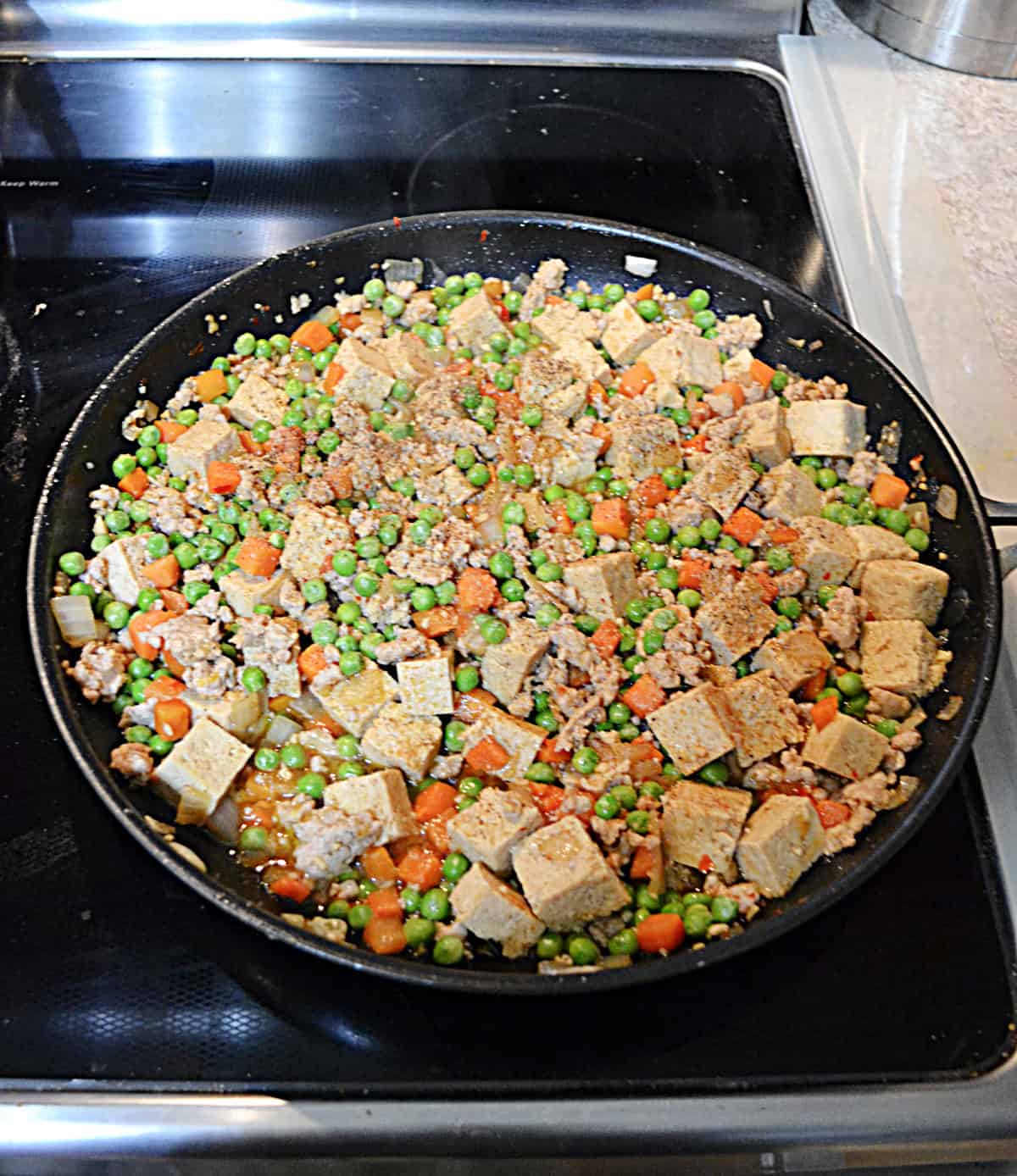 A skillet with tofu, peas, carrots, and pork in it.