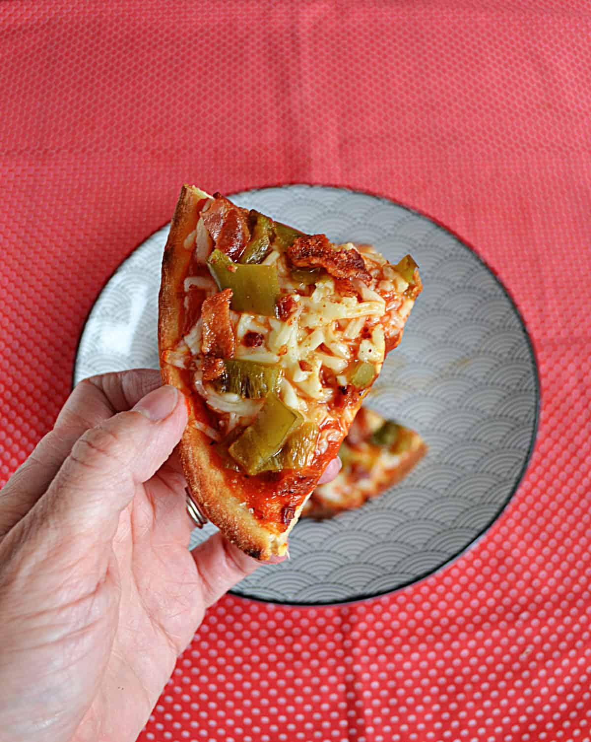 A hand holding a piece of Naan pizza.