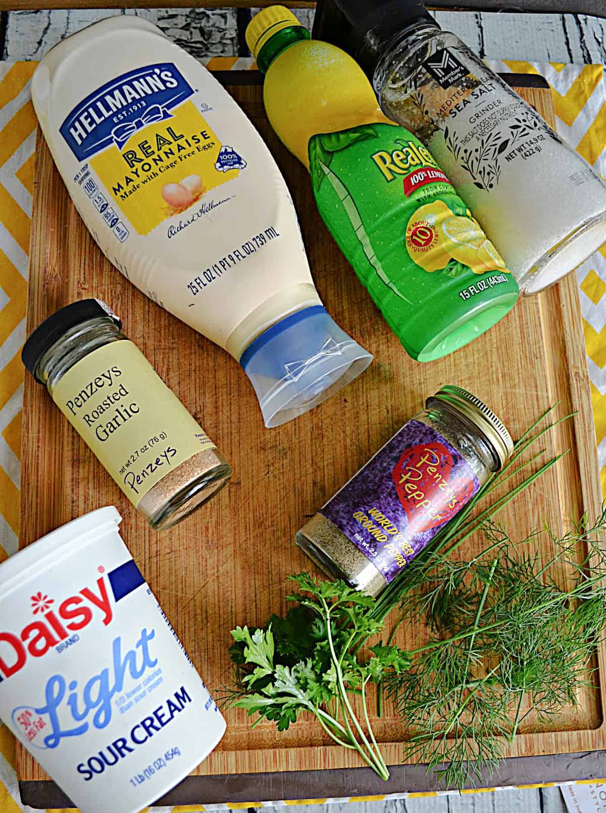 Mayonnaise, lemon juice, alt, pepper, garlic powder, fresh parsley, and fresh dill on a cutting board
