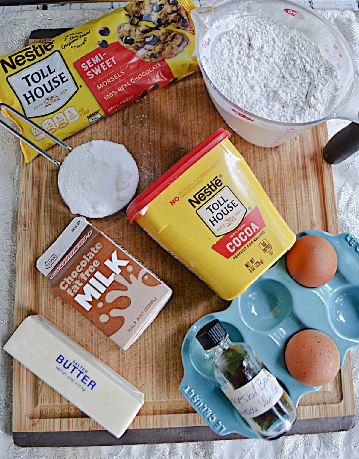 A cutting board with flour, chocolate chips, cocoa powder, eggs, butter, chocolate milk, and sugar on it.