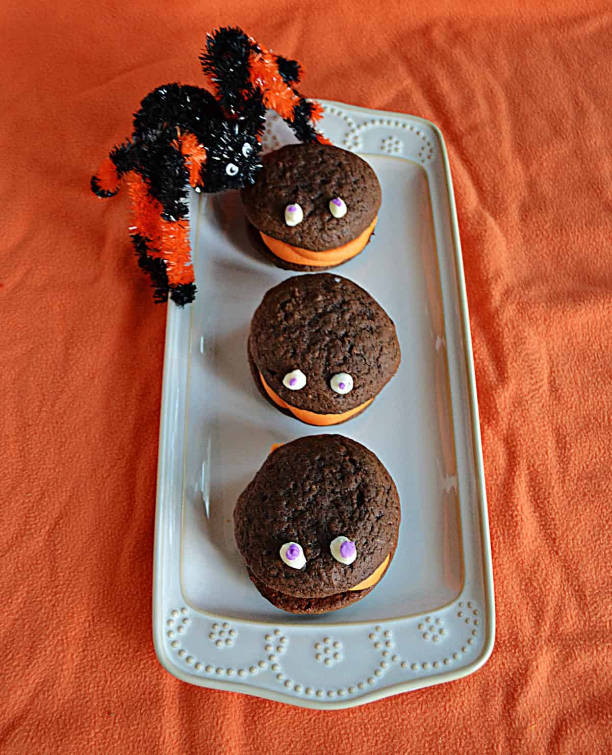 A platter with three chocolate Halloween whoopie pies with eyes on them and a spider.