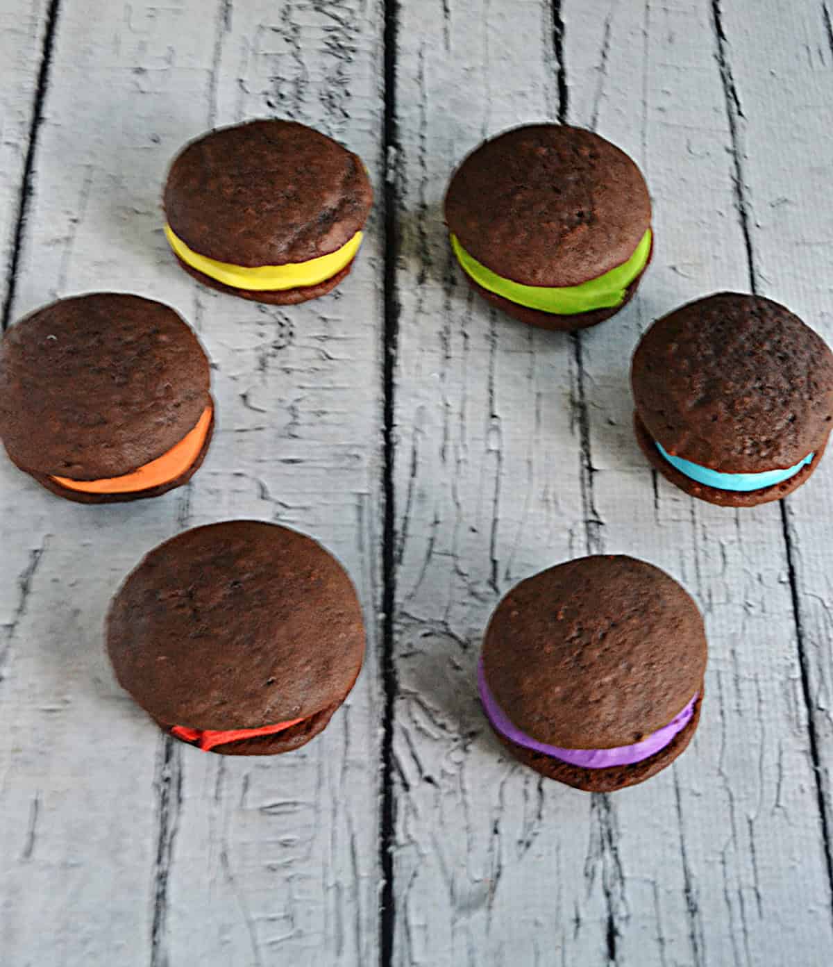 Six chocolate whoopie pies in a circle, each one filled with buttercream in a color of the rainbow.