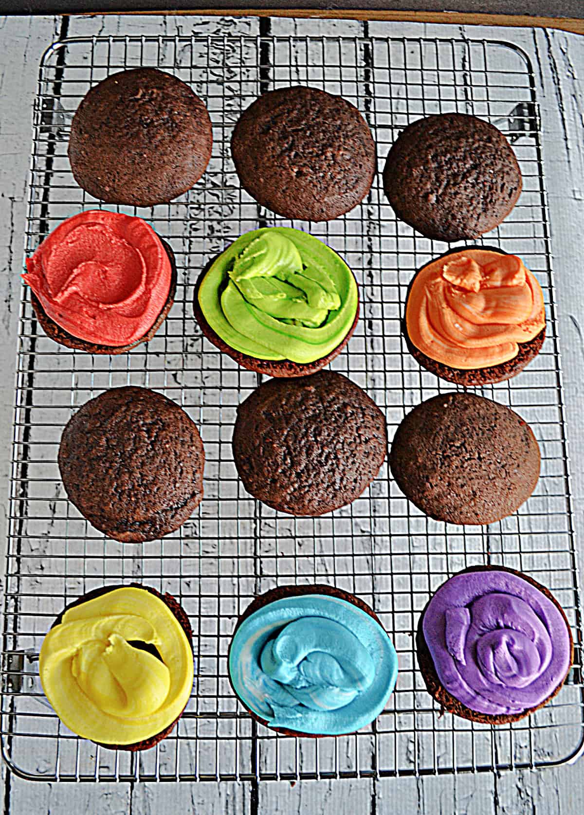A cooling rack with 12 chocolate sandwich cookies, six of them with frosting on them.