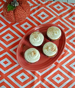 A platter of sweet potato cupcakes with a pumpkin in the background.
