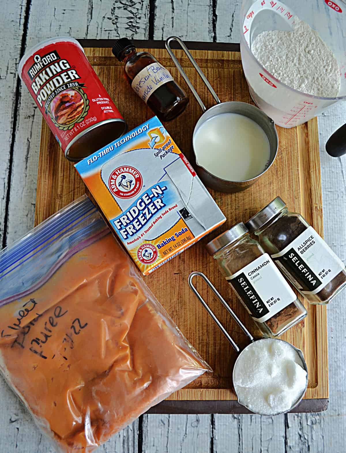 A wooden cutting board with sweet potato puree, baking powder, baking soda, flour, sugar, spices, and oil on it.