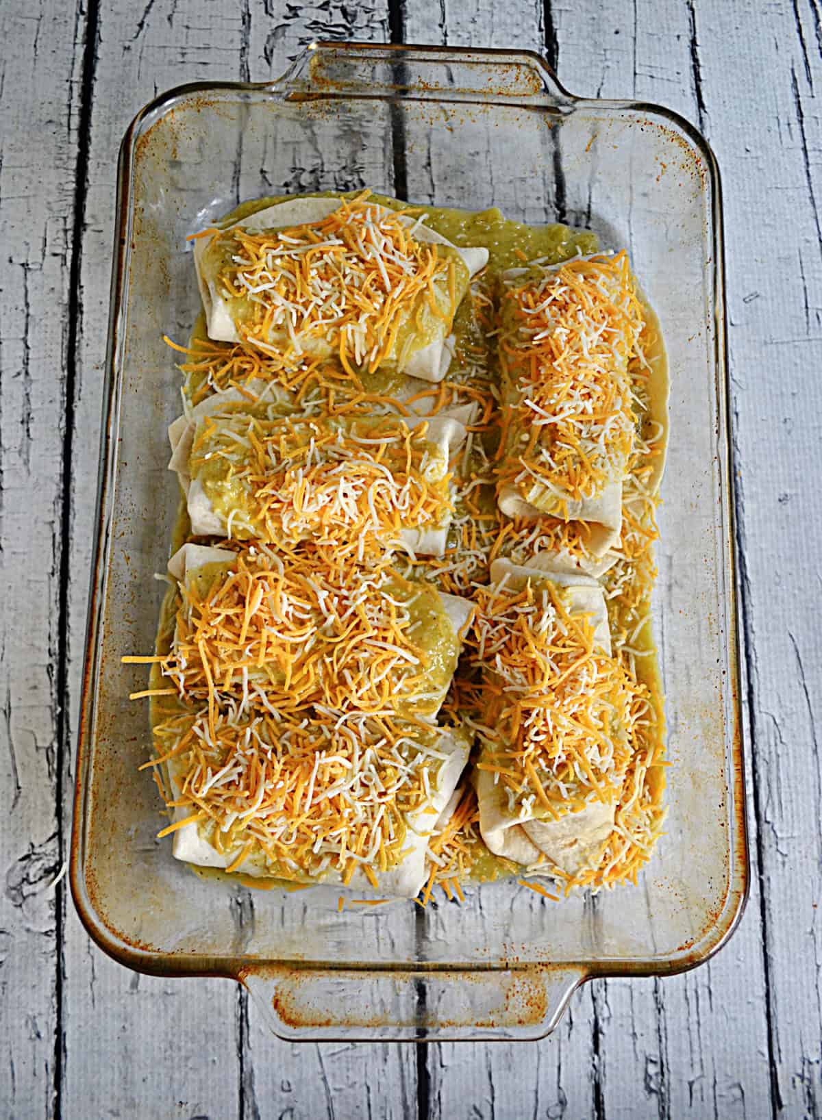A pan of enchiladas with green sauce and cheese on top.