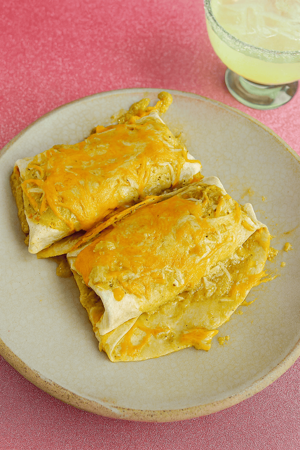 A close up of a plate of enchiladas with a margarita in the background.