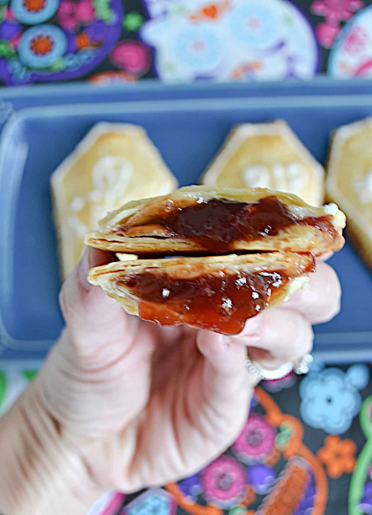 A hand holding a pop tart broken in half with strawberry jam inside.