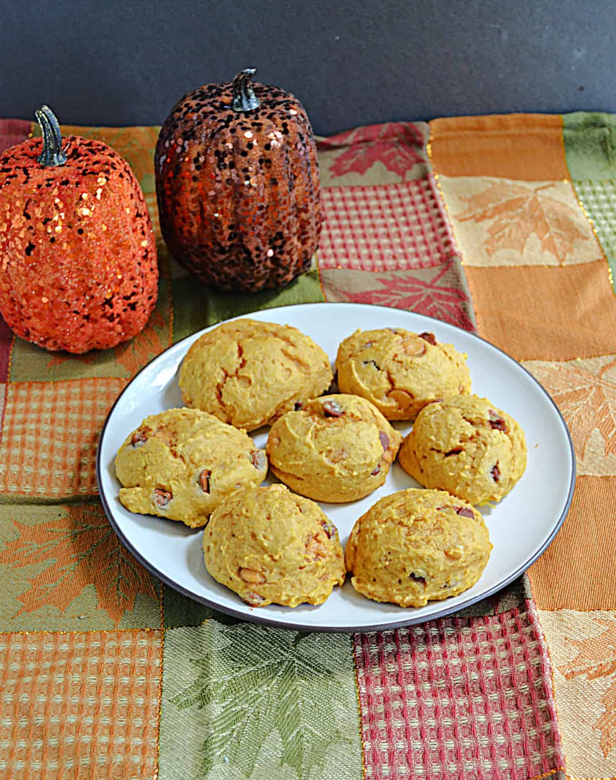 A plate of cookies with two pumpkins behind it.