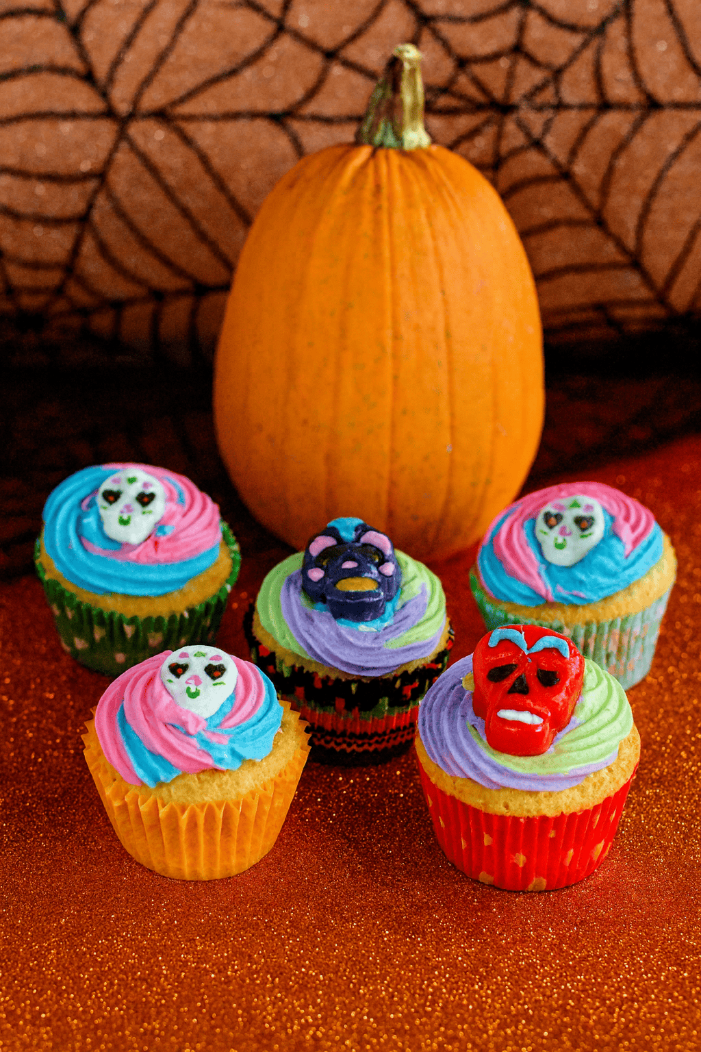 Cupcakes with sugar skulls on top gathered aroun da pumpkin and a giant spiderweb.